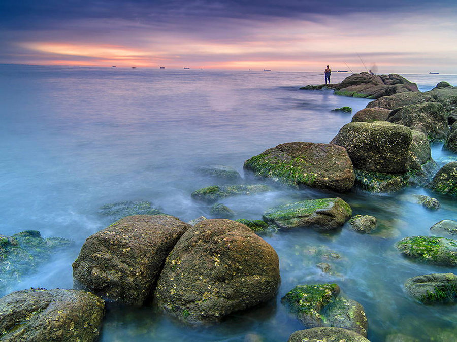 75 0 a fisherman on the rock, facing the sun raise.